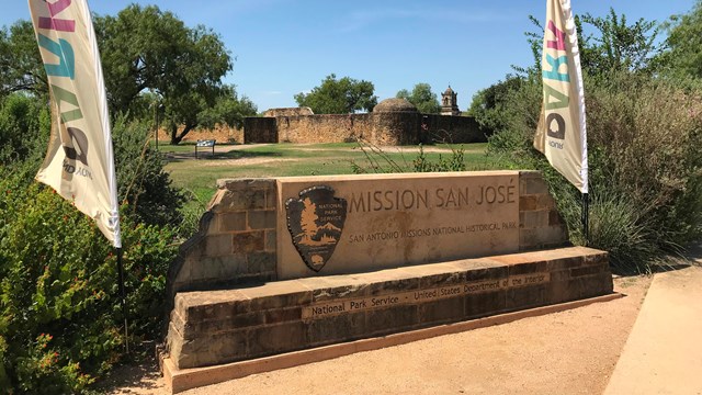 Stone entry sign with "San Jose Mission." Background of an old historic mission building.